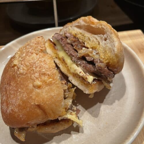 steak sandwiches with pesto, aioli, pesto, brie, and caramelised onions. cut in half to show melted cheese and the steak sandwiches contents