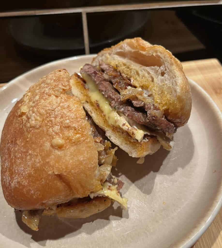 steak sandwiches with pesto, aioli, pesto, brie, and caramelised onions. cut in half to show melted cheese and the steak sandwiches contents