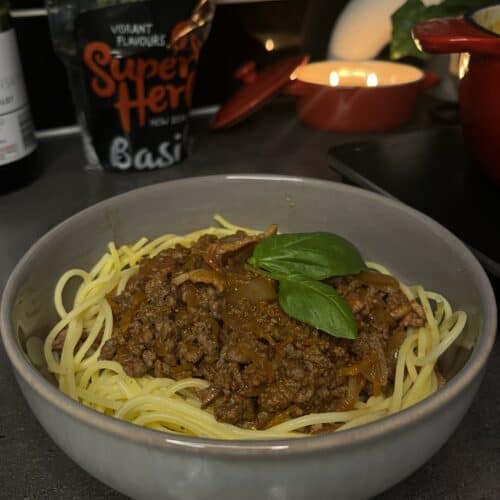 spaghetti bolognese, red wine tomato sauce, bolognese mince in a bowl with gluten free spaghetti with fresh basil and candles in the background