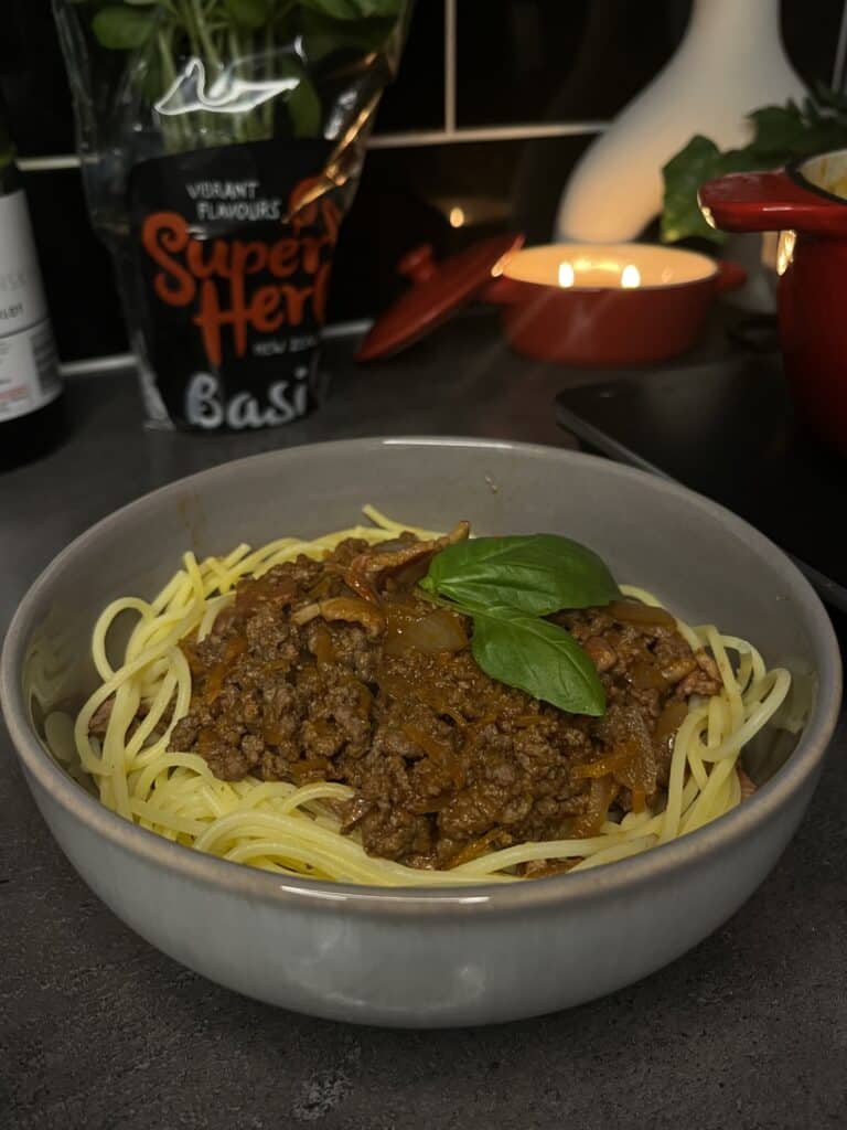 spaghetti bolognese, red wine tomato sauce, bolognese mince in a bowl with gluten free spaghetti with fresh basil and candles in the background