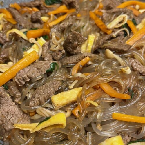 korean vermicelli japchae dish, chewy translucent noodles with carrot, egg, onion, enoki mushroom in soy sauce