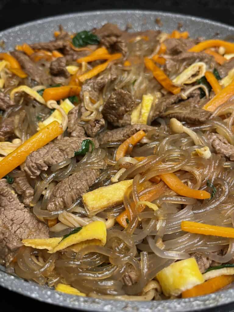 korean vermicelli japchae dish, chewy translucent noodles with carrot, egg, onion, enoki mushroom in soy sauce