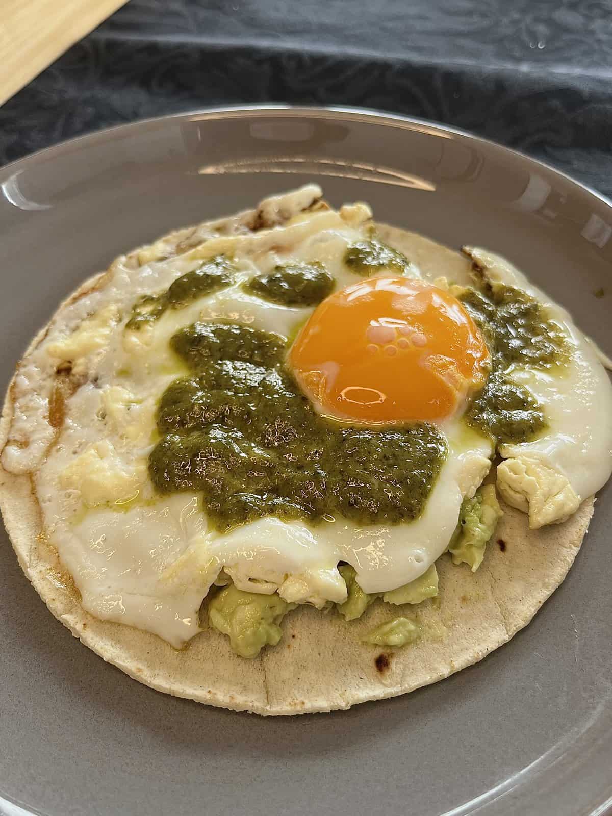 toasted tortilla with feta, fried egg, runny yolk, aioli, and smashed avocado, making pesto feta eggs