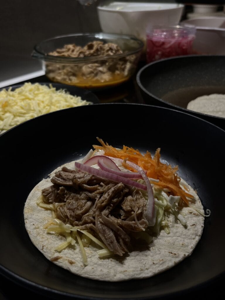 pulled pork tacos, cheese, pickled red onions, grated carrot, and cabbage coleslaw, on a corn tortilla